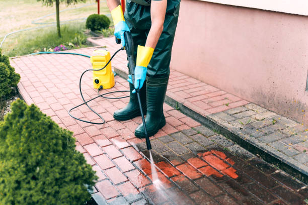 Technician pressure washing a red brick patio